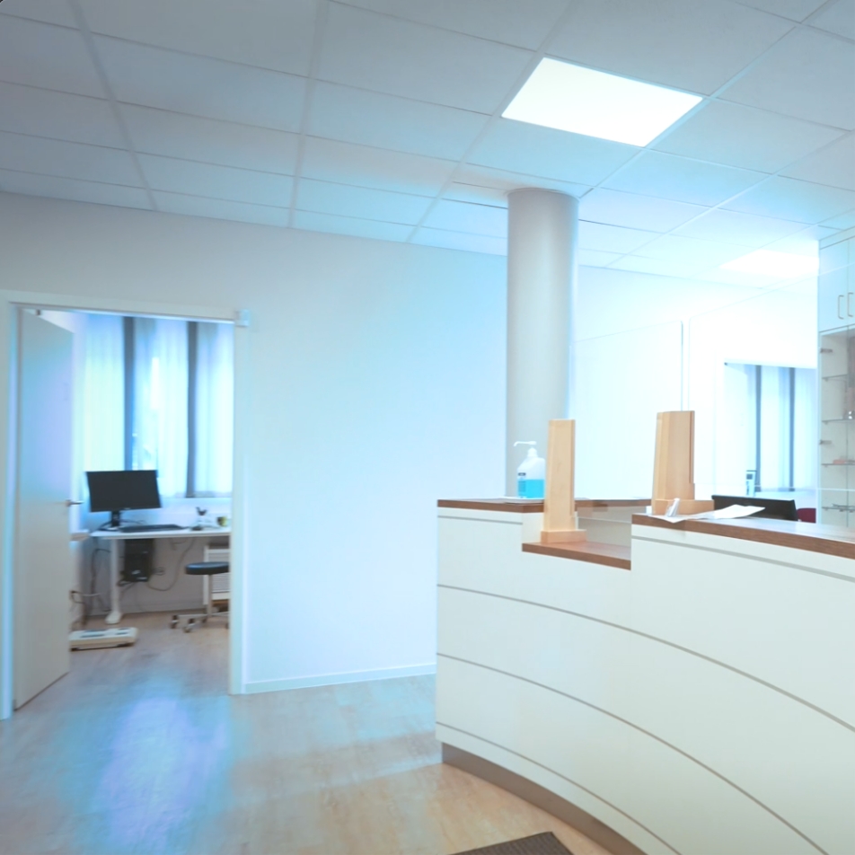 Heller Empfangsbereich mit einer Empfangstheke und einem angrenzenden Büro. Fenstereinblick und moderne Ausstattung.